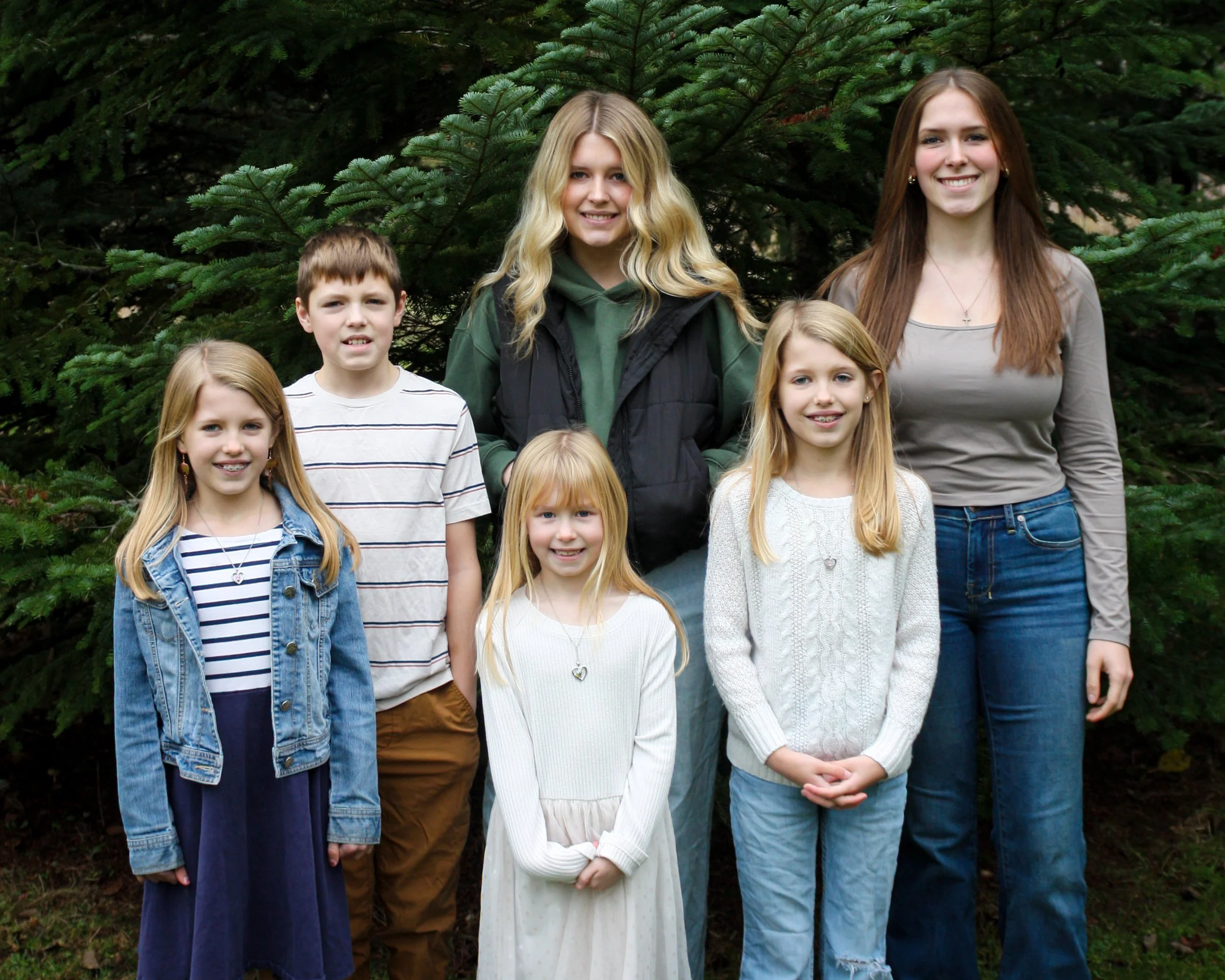 A portrait of six people, including the "Kitten Socializing Team, standing outdoors in front of evergreen trees.