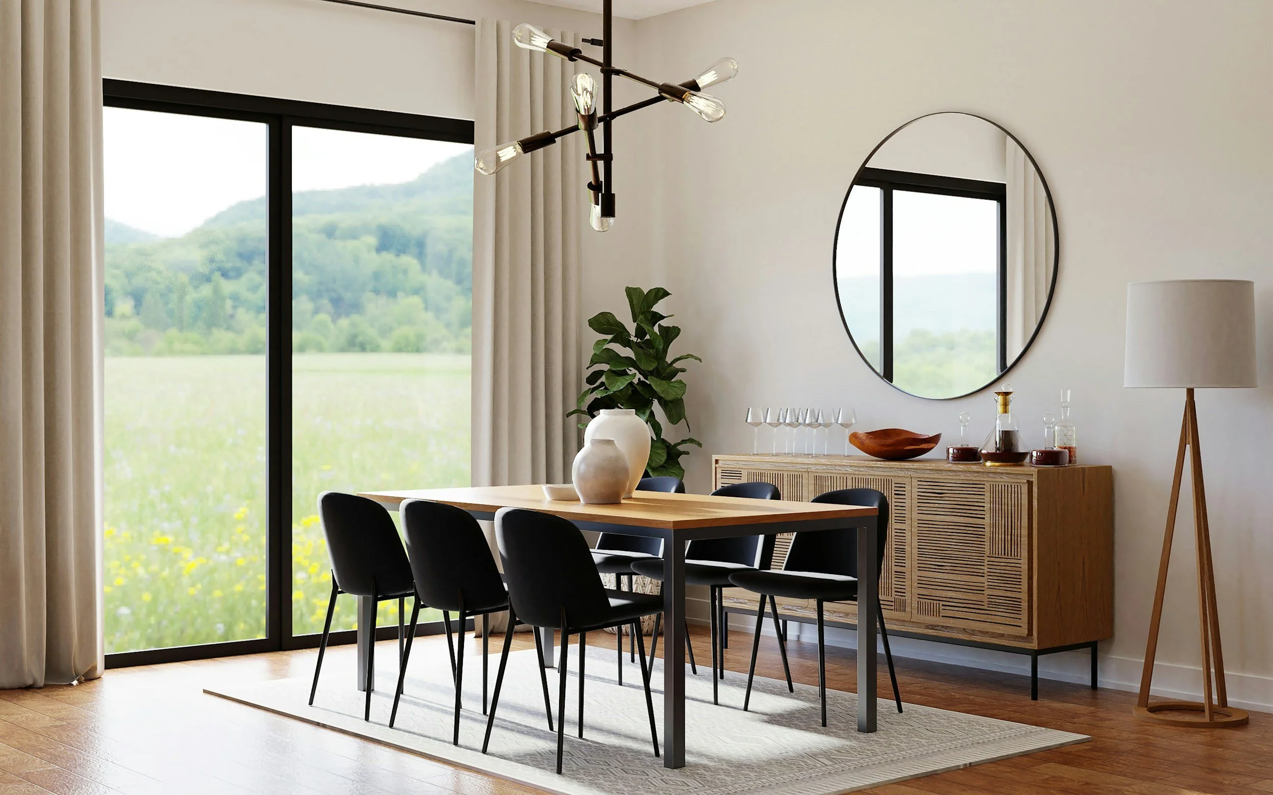A modern dining room with a wooden table and six black chairs. A large window with cream curtains shows a scenic view of green hills and trees. A round mirror hangs on the white wall, reflecting part of the room. A sideboard with decorative items, in