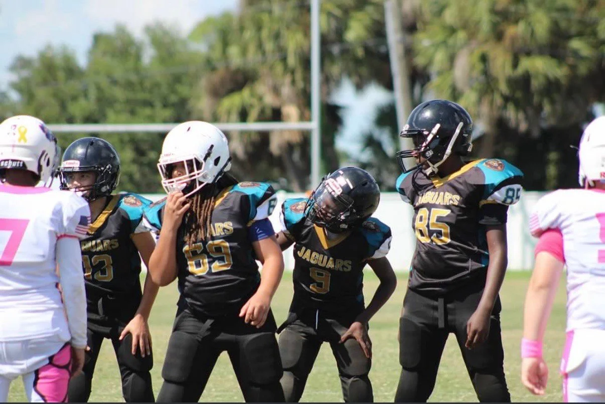 Youth football players in black and white jerseys lined up on the field during a game.