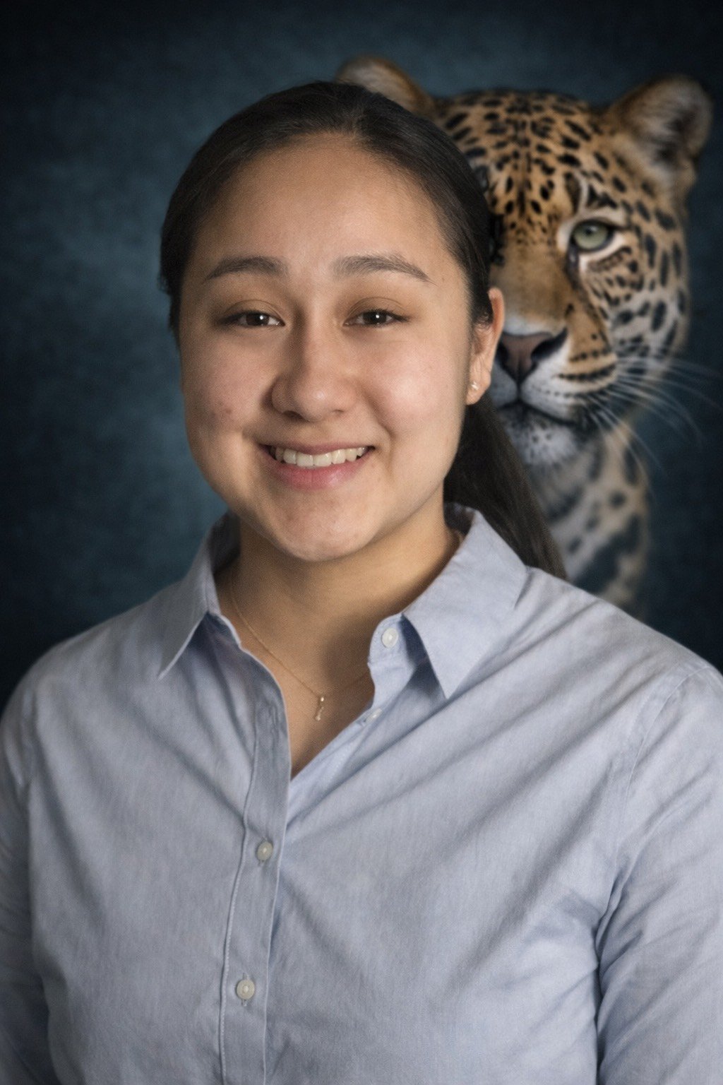 A young woman smiling in front of a dark backdrop with a large image of a jaguar behind her.