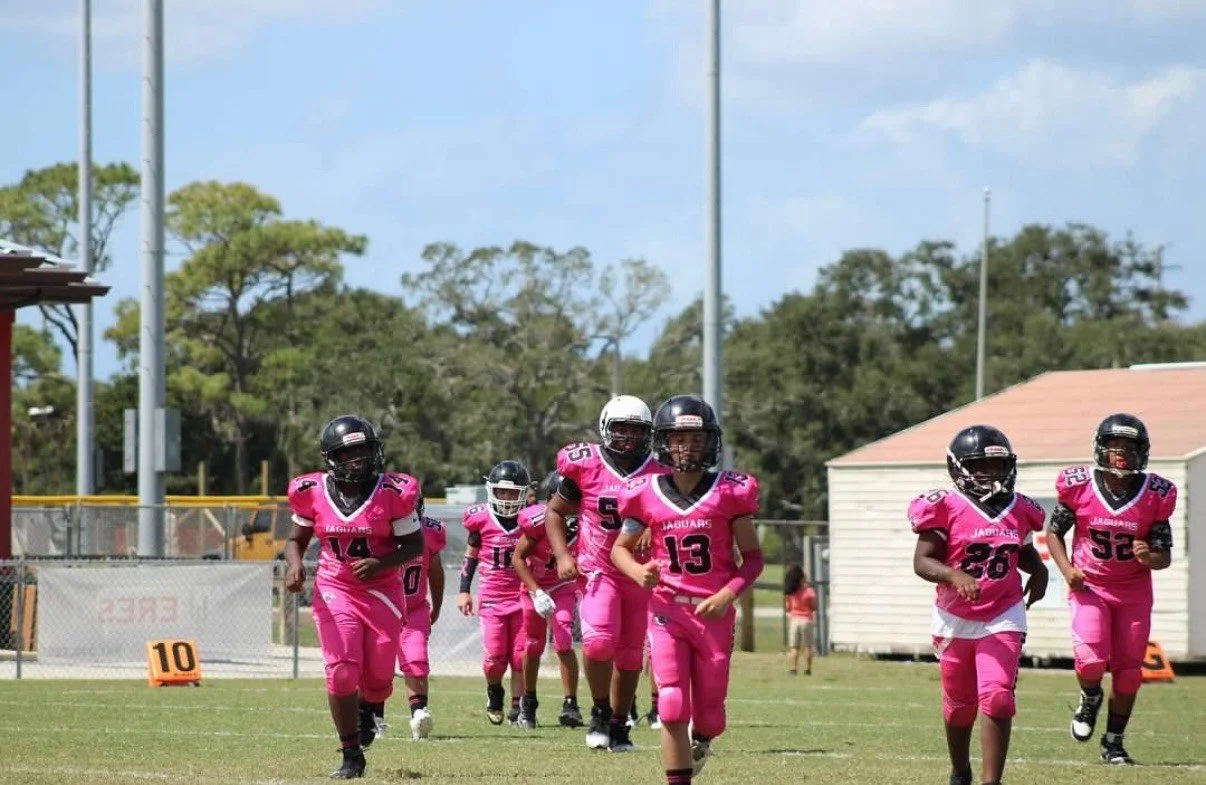 Young football players in pink jerseys running onto the field.