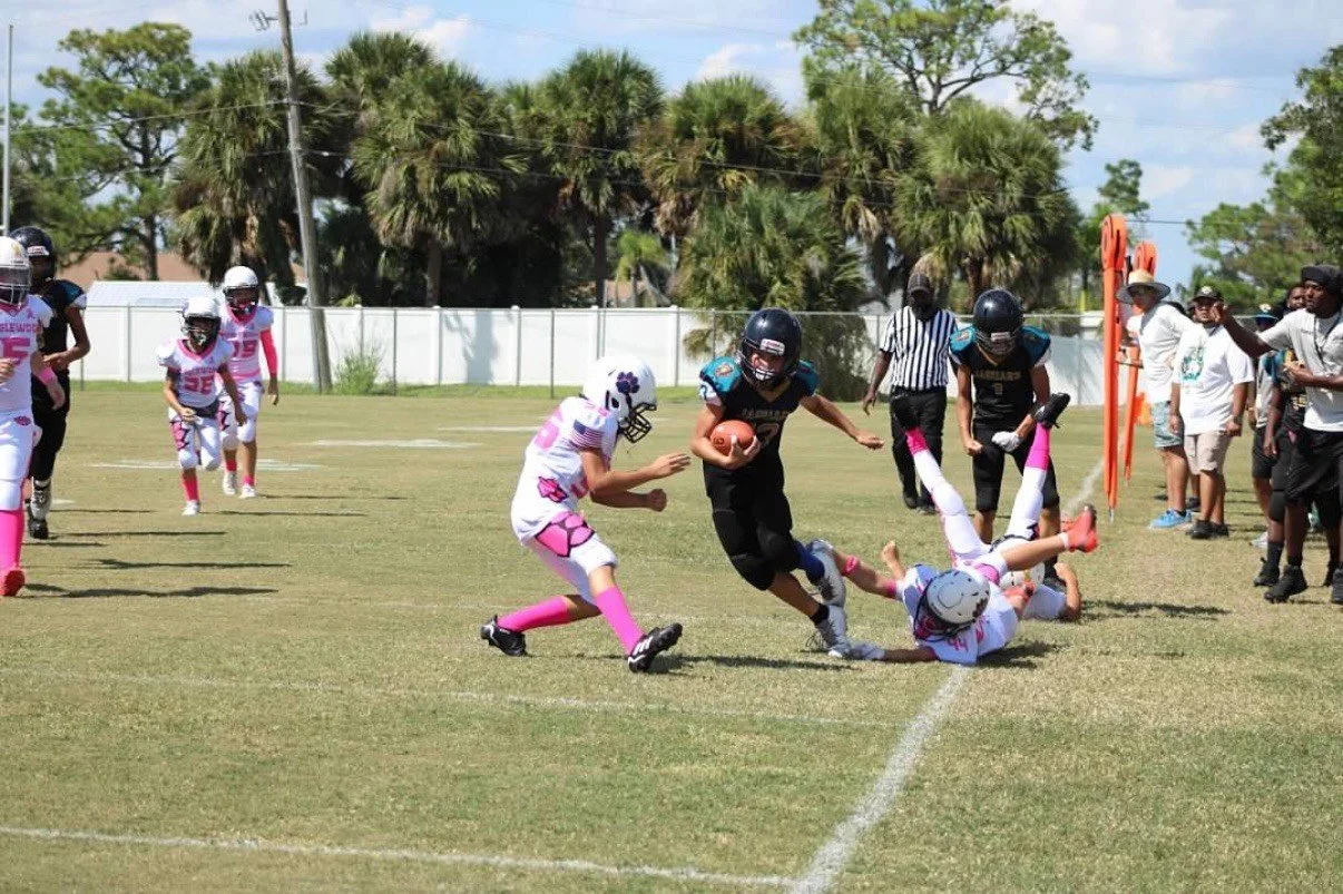 Youth football game, with a player running with the ball past defenders and another player on the ground during play.