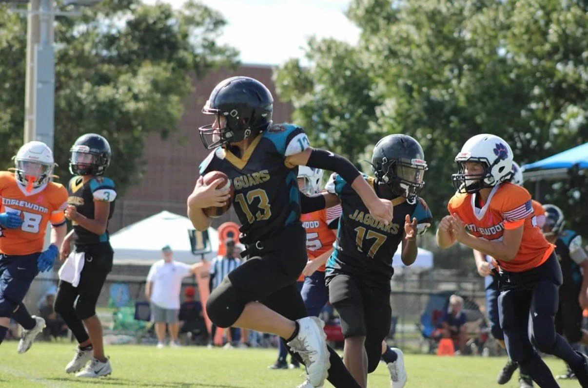 Young football players in helmets and uniforms playing on a field during a game. Manatee Jaguars football 