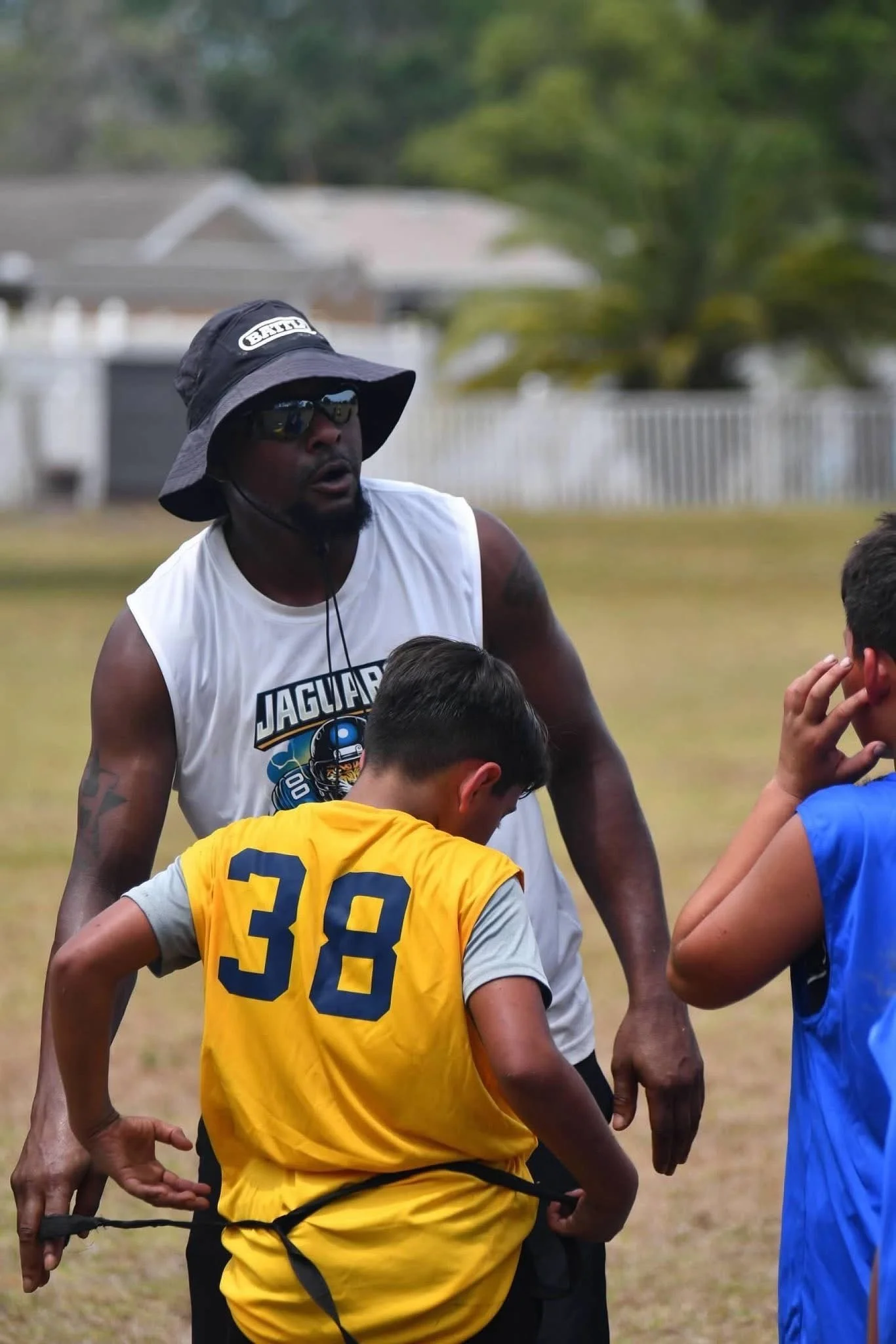 Adult football coach talking to two young players during practice outside.
