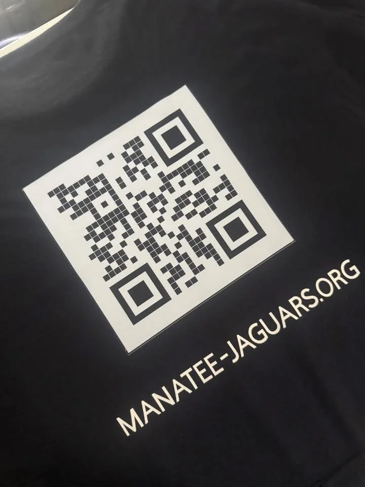 A QR code on a black surface with the website URL 'MANATEE-JAGUARS.ORG' printed below it.