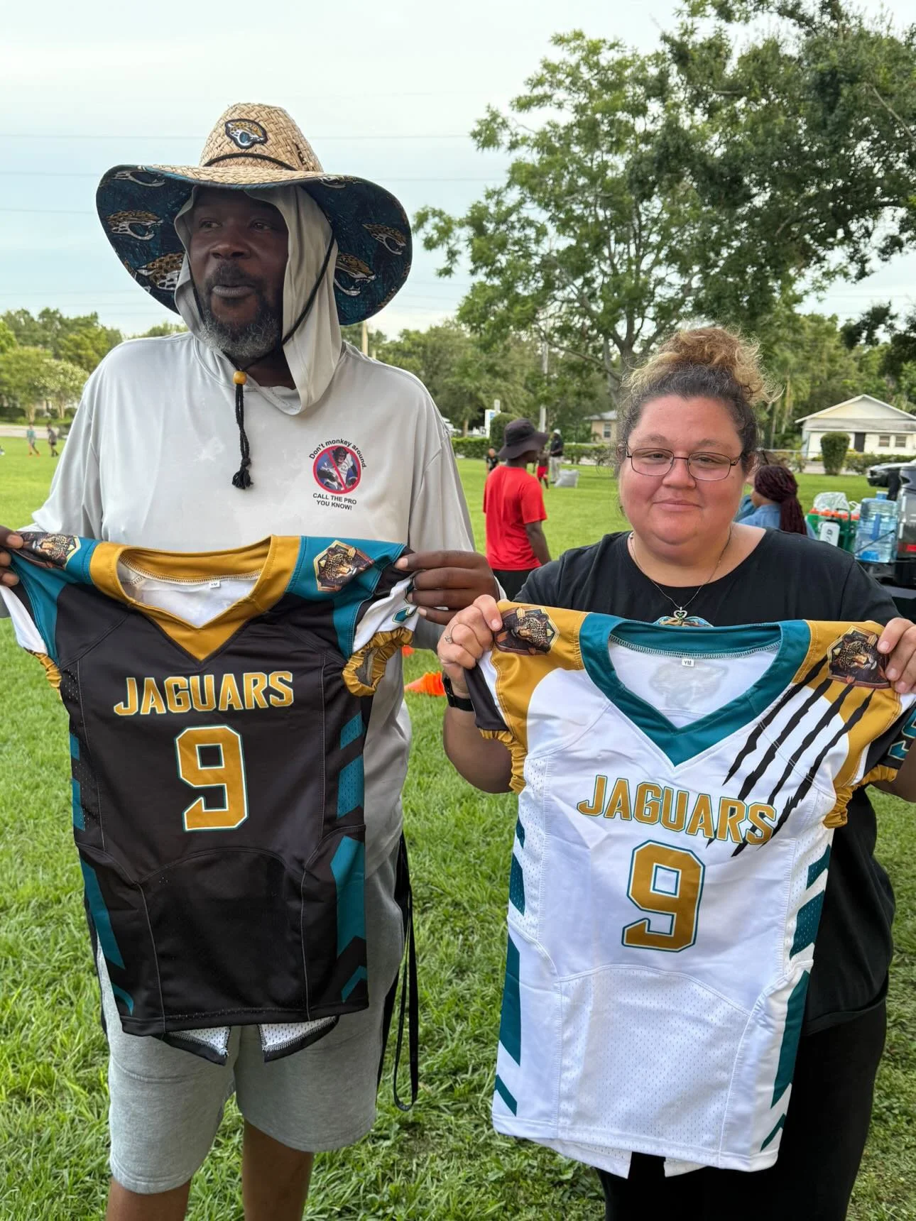 Two people holding Jaguars football jerseys, standing in a park.
