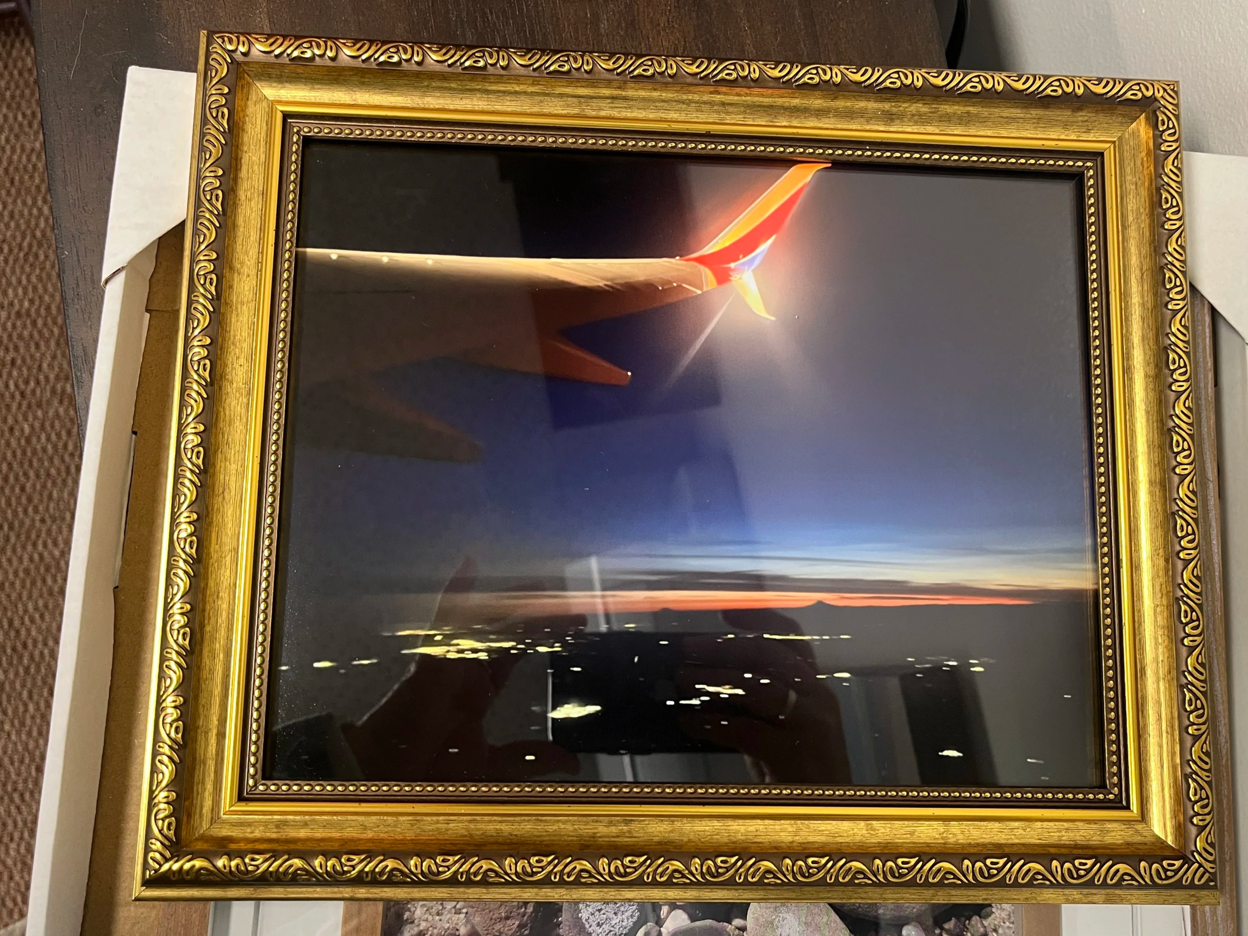 Photo taken from airplane window at dusk.  A dark blue sky with oranges and red on the horizon with a bright light on the wing tip highlighting the orange and red paint on the wing.  City lights below are blurred showing the speed of the plane.