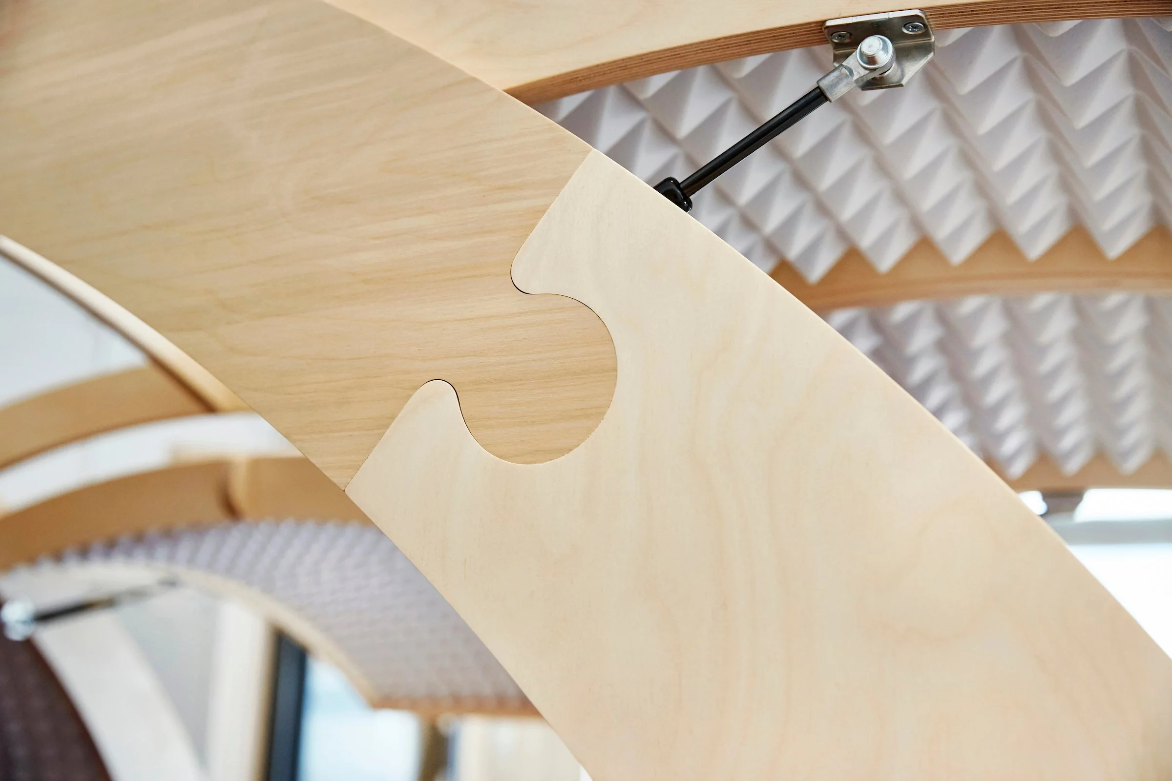 Close-up of a wooden desk with a cut-out section, a mechanical arm, and soundproofing foam panels in the background.