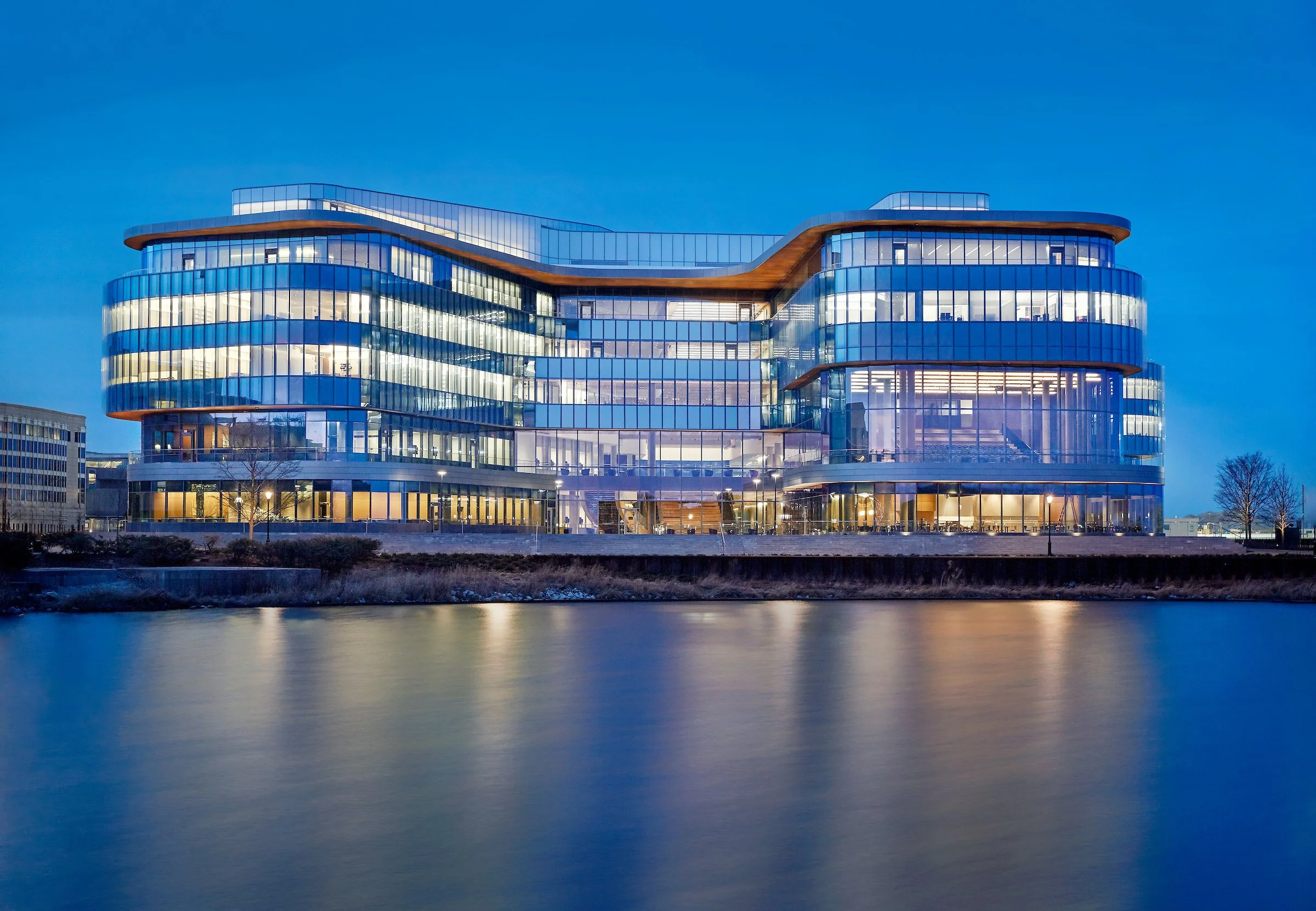 Modern glass office building reflecting on water with a clear evening sky in the background.