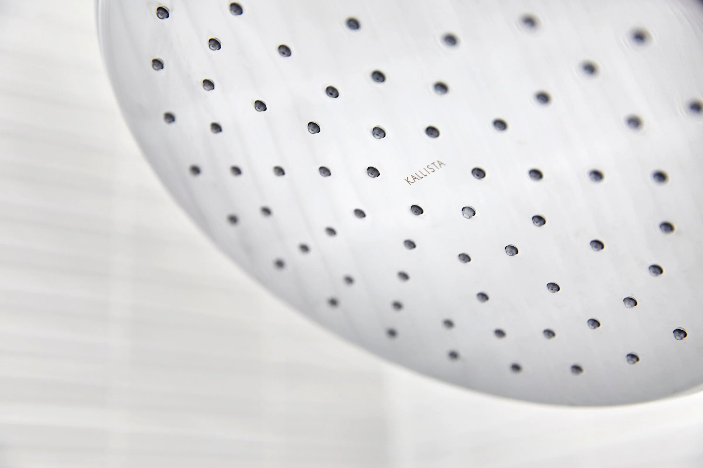Close-up of a white showerhead with multiple black nozzles, brand labeled 'KALLISTA.'