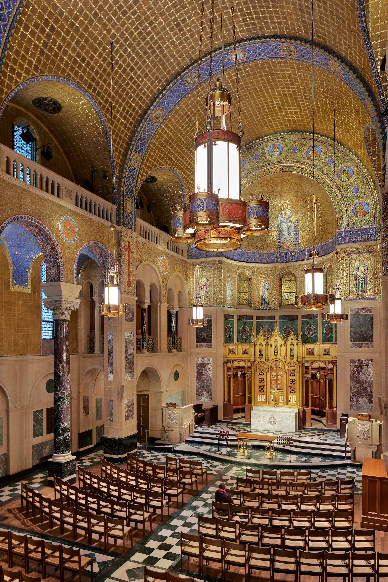 Interior view of a church with gold decorated ceiling, chandeliers, religious icons and an altar.