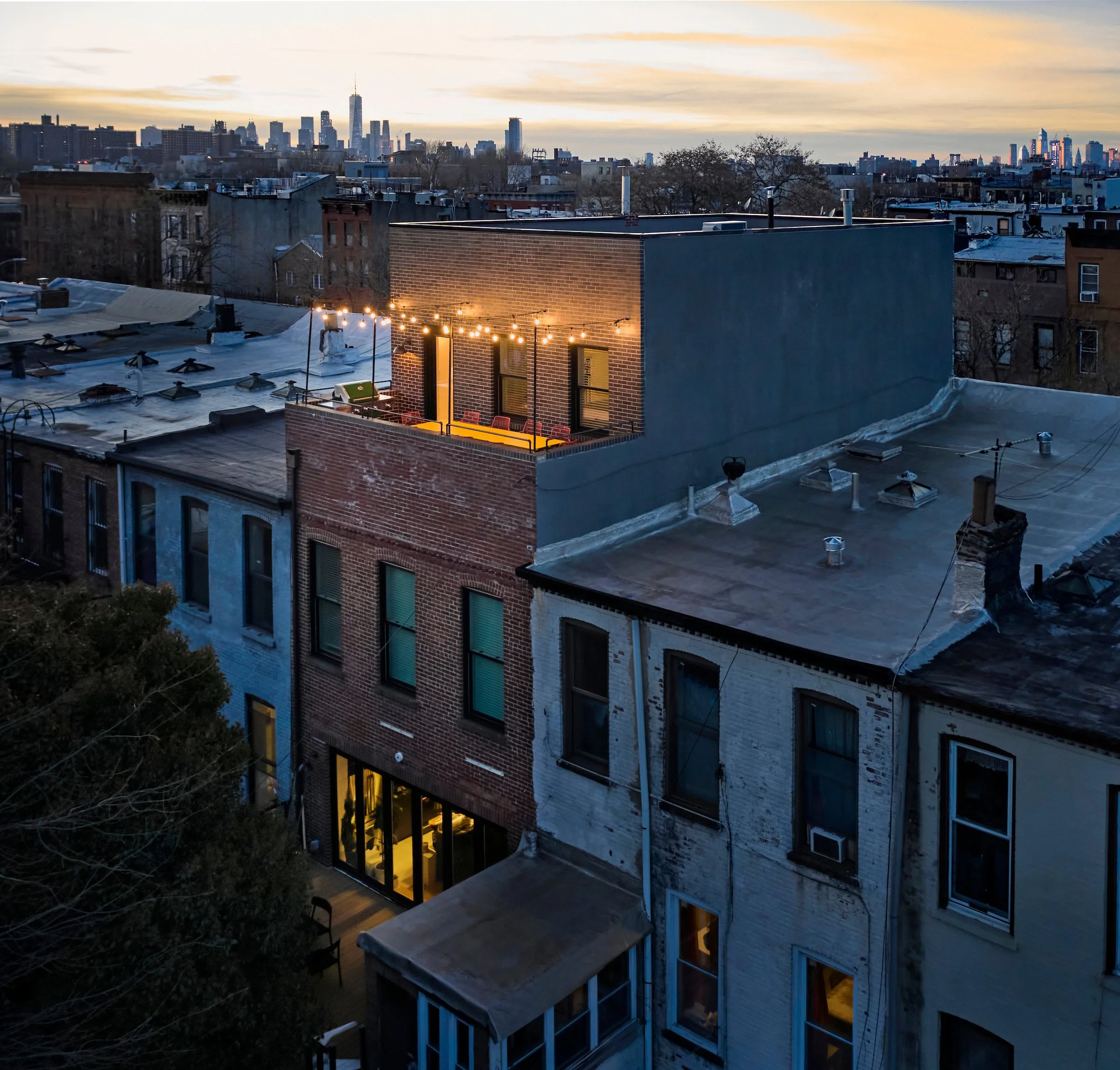 Urban rooftop with string lights, patio furniture, and city skyline at dusk