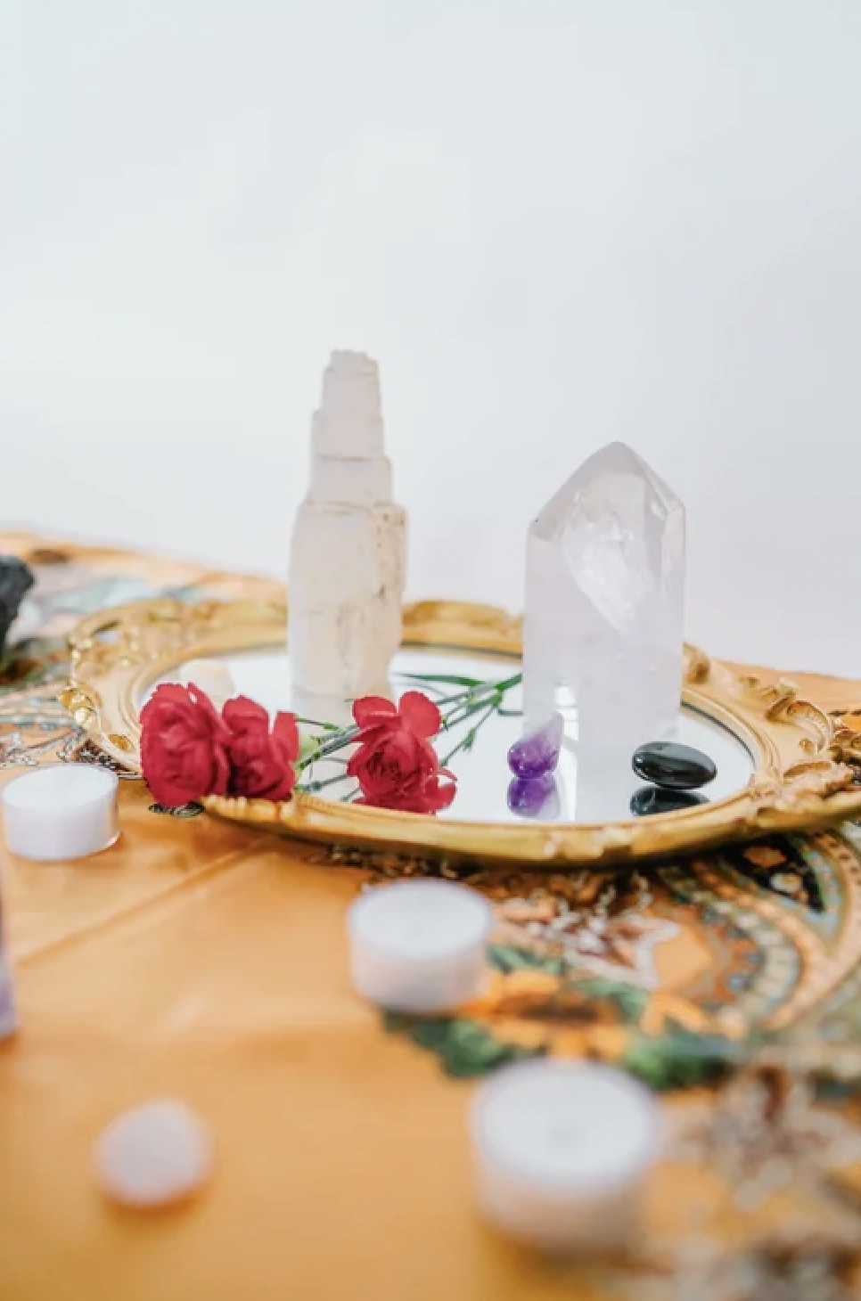 Tarot prep with an amethyst stone, and other crystals, surrounded by red flowers and tea light candles on an embroidered cloth.