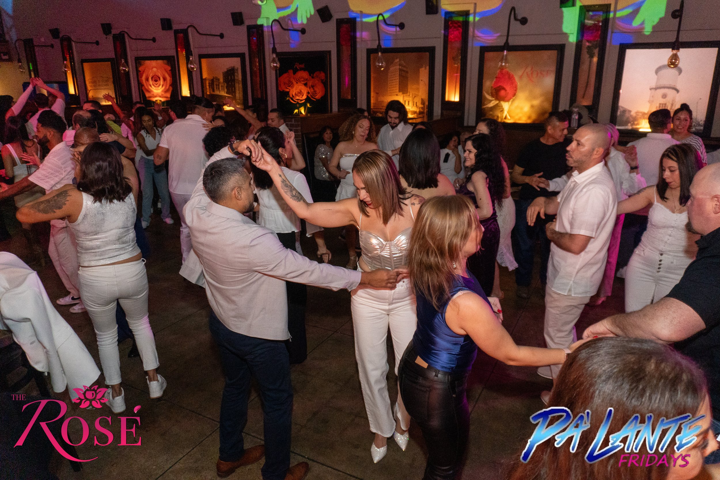 People salsa dancing and socializing at a lively party or nightclub with colorful wall decorations and framed pictures.