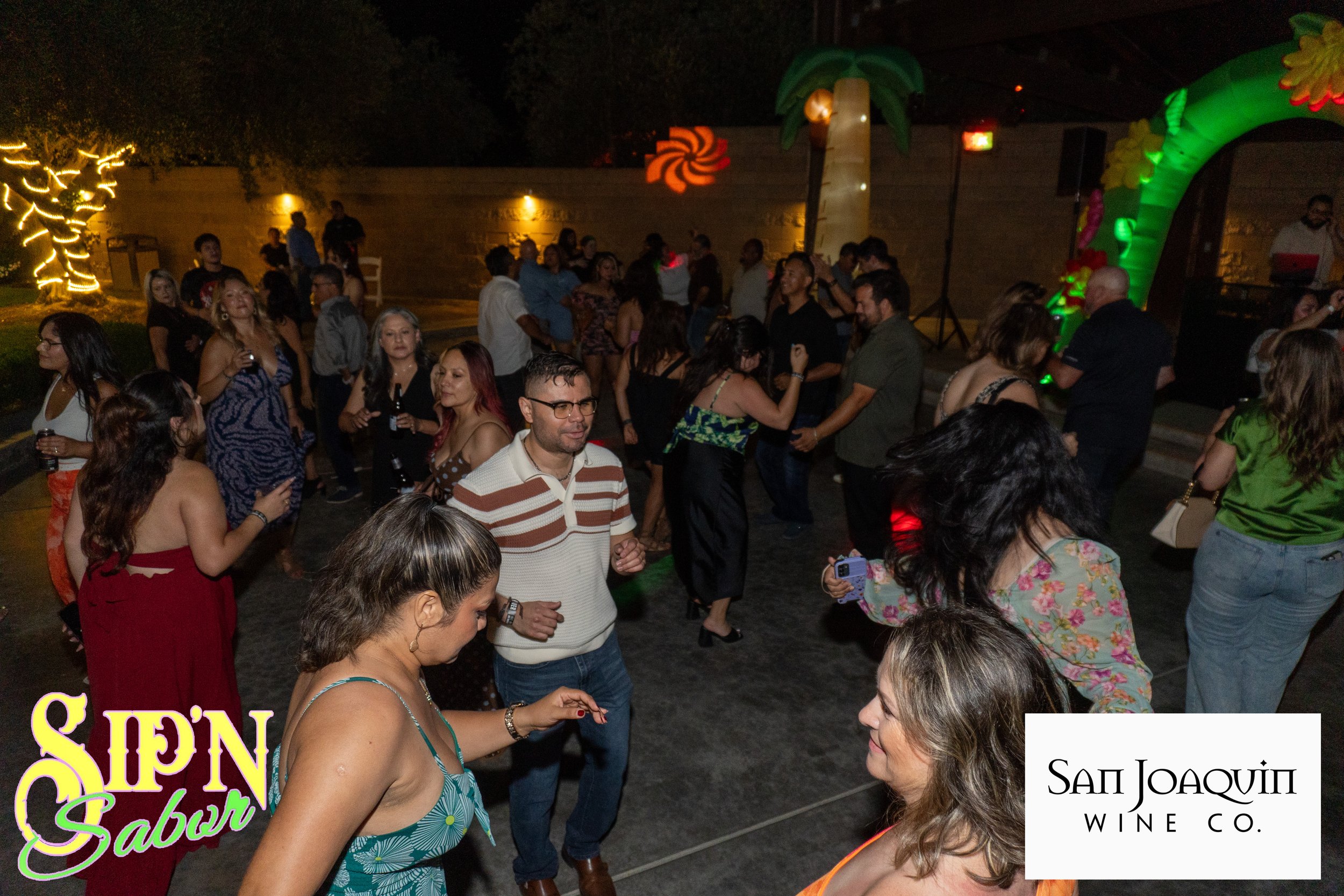 People Salsa dancing and socializing at a lively indoor event with string lights and wooden decor, some smiling and engaging in conversations.