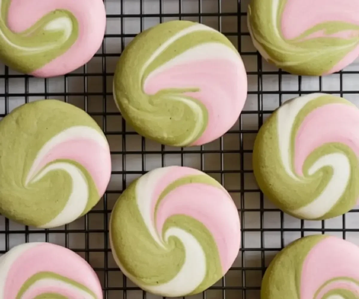 Swirled cookies with pink, white, and green marbled icing on a black cooling rack.