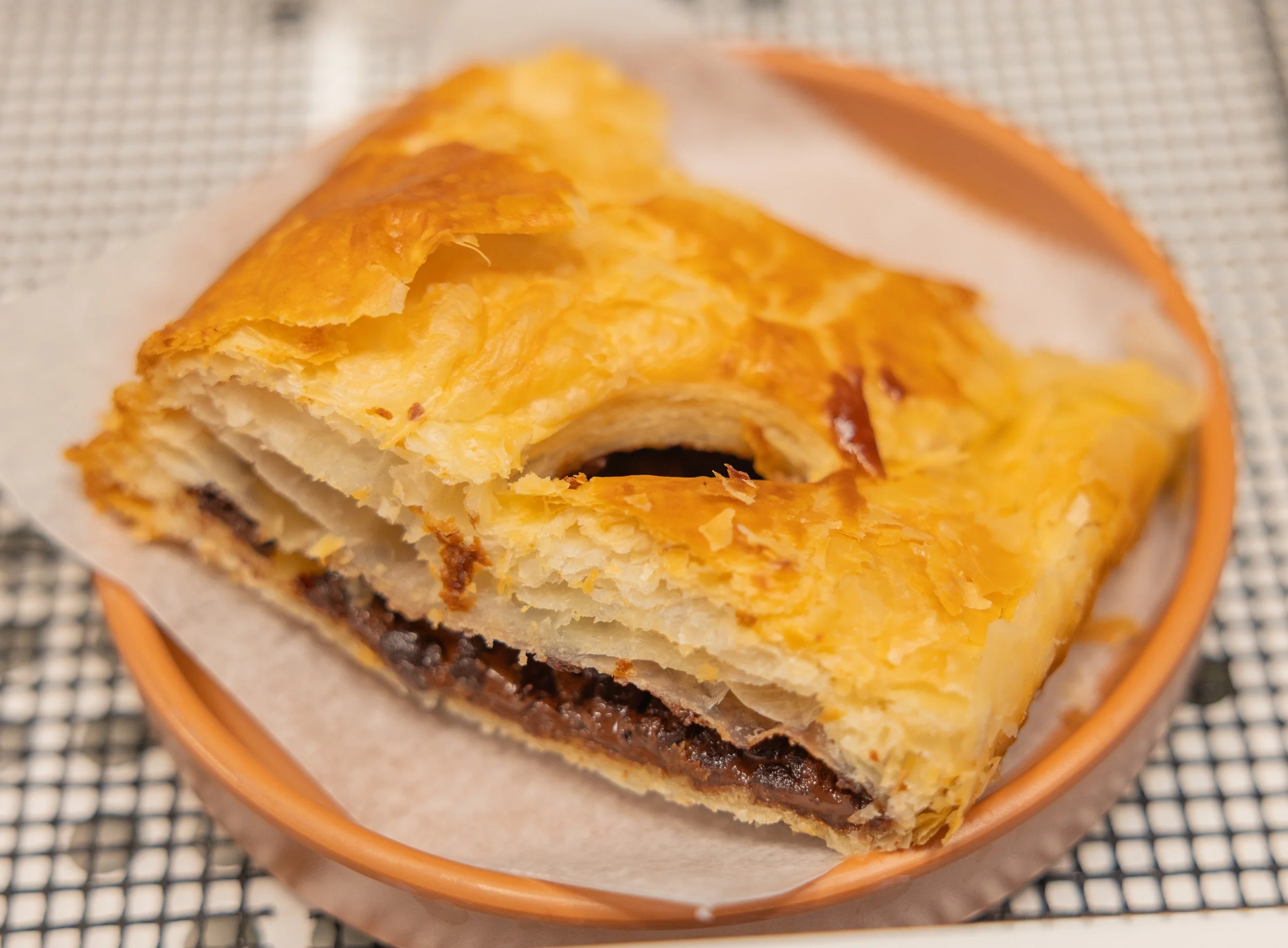 A close-up view of a freshly baked cinnamon roll inside a small orange dish on a checkered surface.