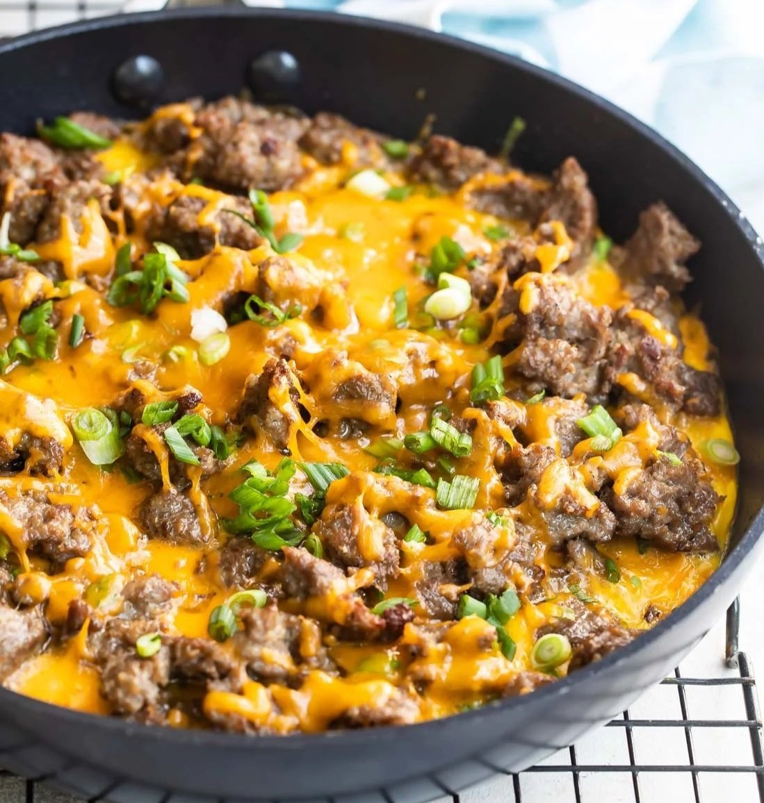 Cheesy beef taco skillet with ground beef, melted cheddar cheese, and chopped green onions in a black skillet.