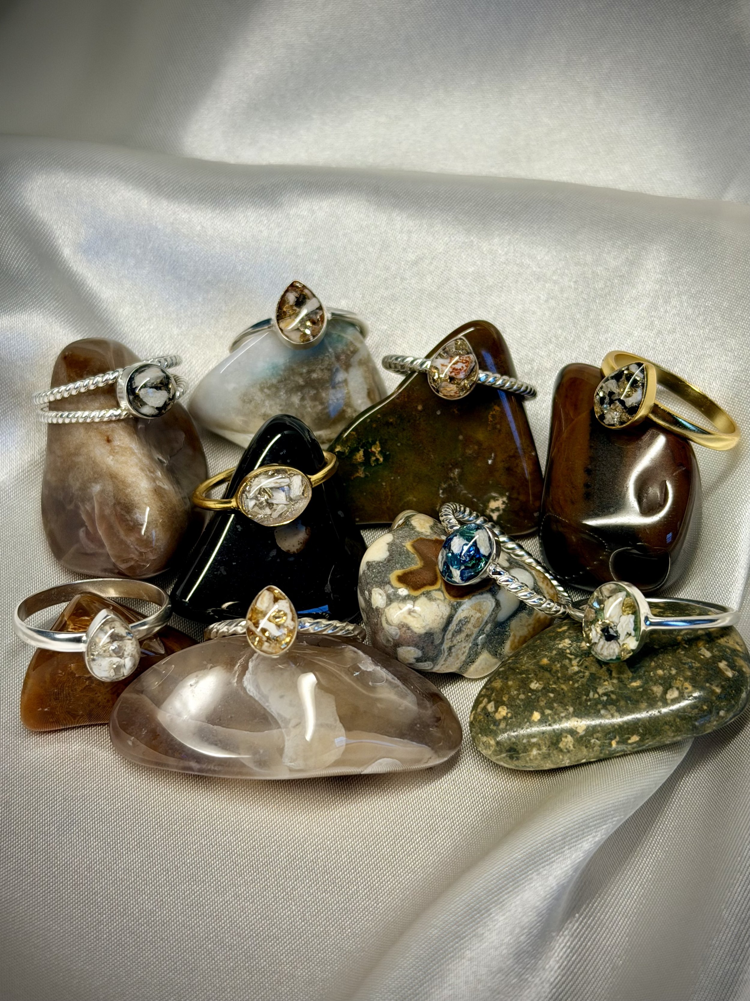 Collection of various gemstone rings with different colored stones, displayed on a silky fabric background.