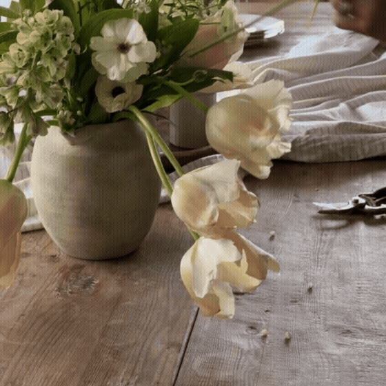 A bouquet of white and green flowers in a gray vase on a wooden table.