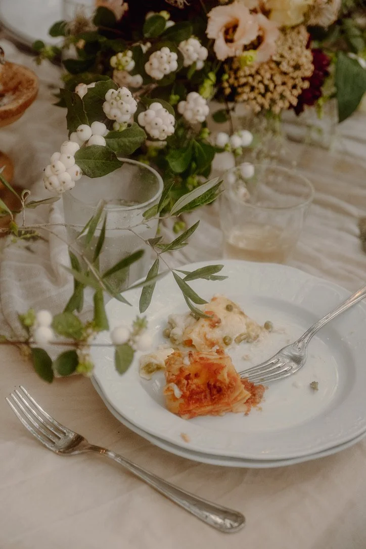 Partially eaten plate of lasagna with a fork, on a dinner table decorated with floral arrangements and candles.