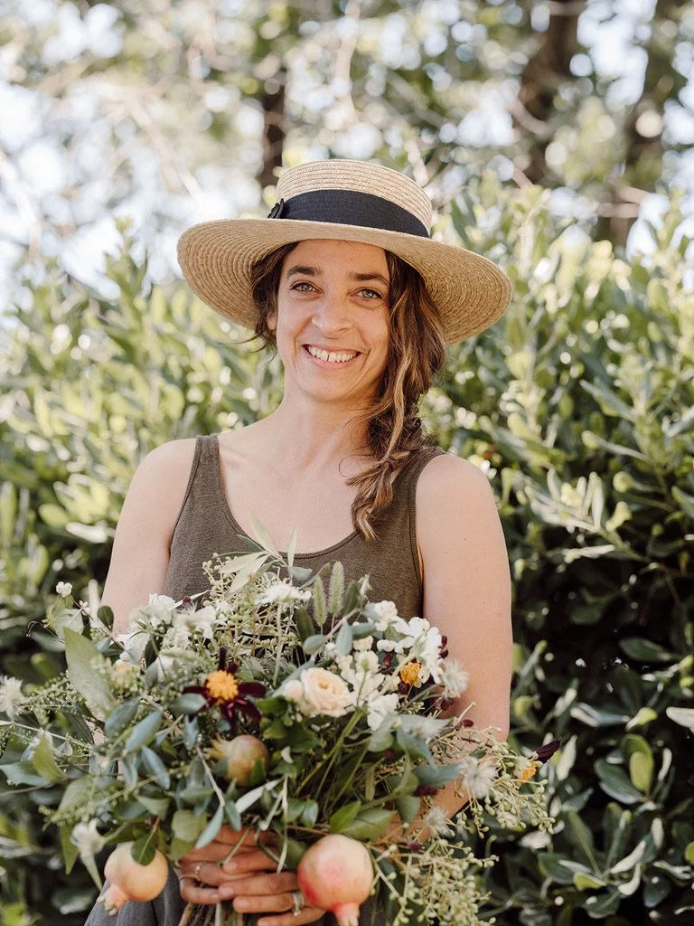 Teressa Johnson smiling and holding a bouquet of flowers outside in a lush green garden.