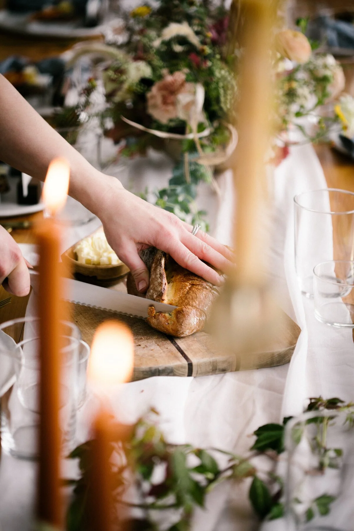 Person carving a roasted ham at a decorated dinner table with flowers and lit candles.