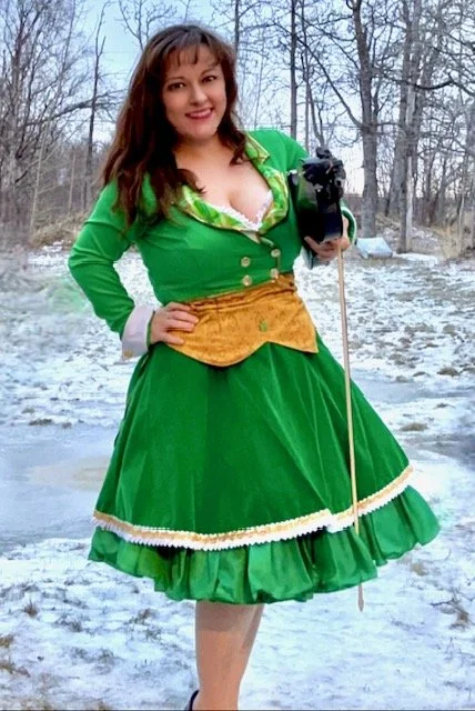Woman in a green dress holding a camera outdoors on a snowy day.