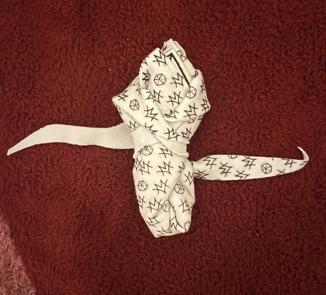 A white fabric item with black comic-style symbols like lightning bolts, dice, and X's, placed on a red textured blanket.