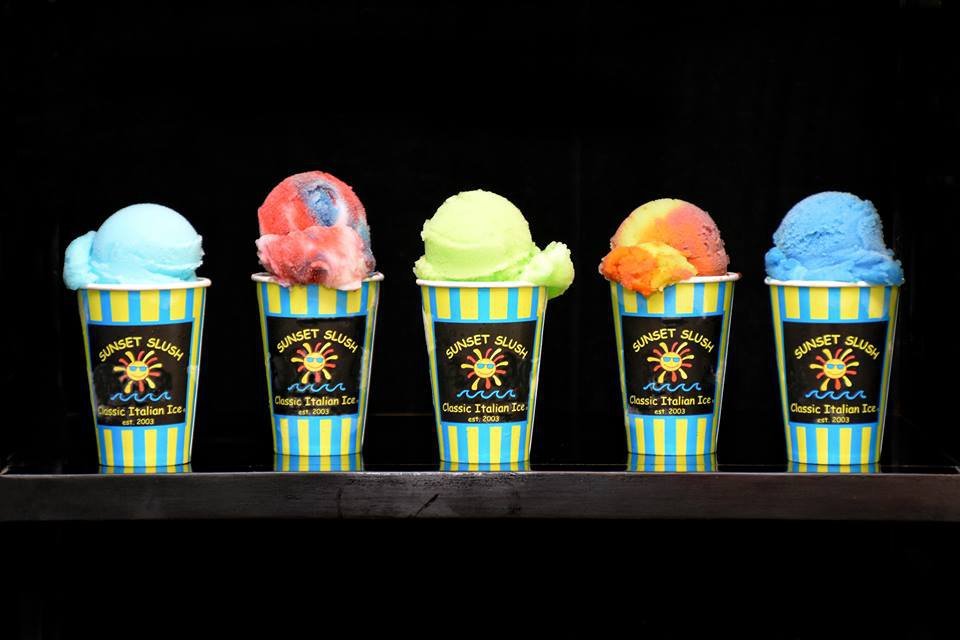 Five cups of colorful ice cream with different flavors on a black background, each cup labeled 'Sunset Slush, Classic Italian Ice, est. 2003.'