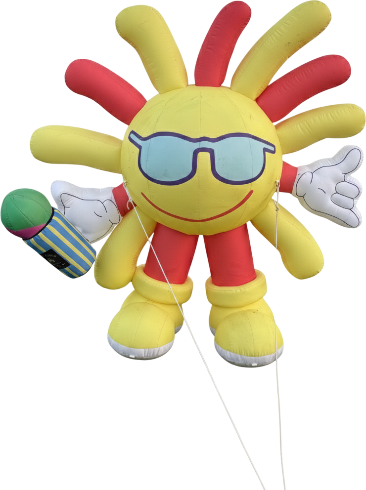 A colorful inflatable character resembling a sun with a smiling face, sunglasses, and rays in red and yellow. It has cartoon gloves on its hands, one holding a microphone. The character has a cheerful, friendly appearance.