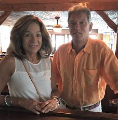 A woman and a man standing together in an indoor setting, possibly a restaurant, with wooden beams and a ceiling fan visible in the background.