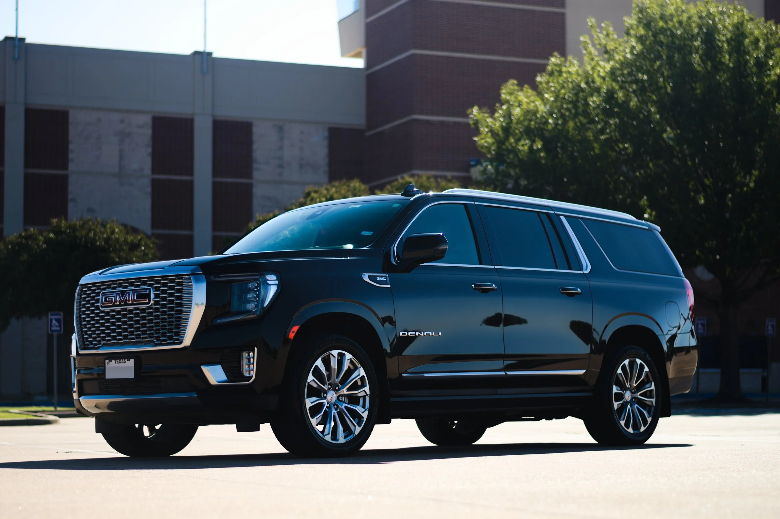 A black GMC Denali SUV parked outdoors on a sunny day with trees and a building in the background.