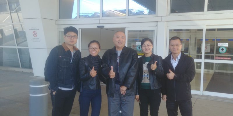 Five people standing outside an airport entrance, all giving thumbs up.