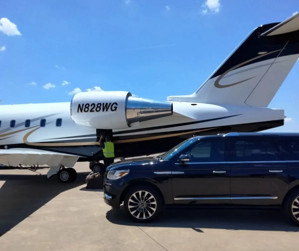 Black luxury SUV parked on tarmac with a private jet in the background under a blue sky.