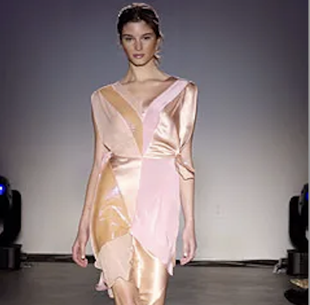 A woman walking on a runway wearing a pink and peach-colored satin dress with a V-neck and long sleeves.