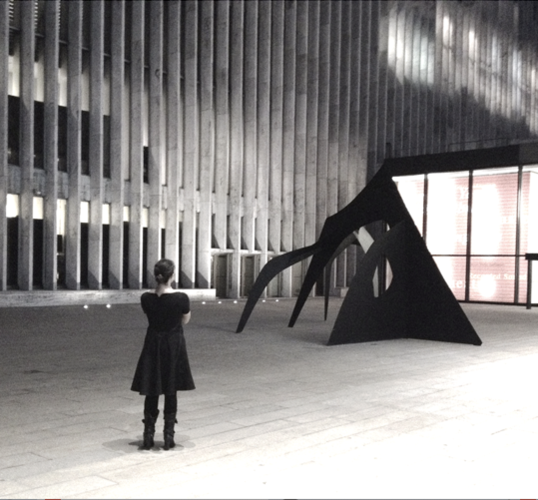 A woman in a black dress stands in an empty indoor space, looking at a large abstract black sculpture near a glass window with a red and white sign behind.