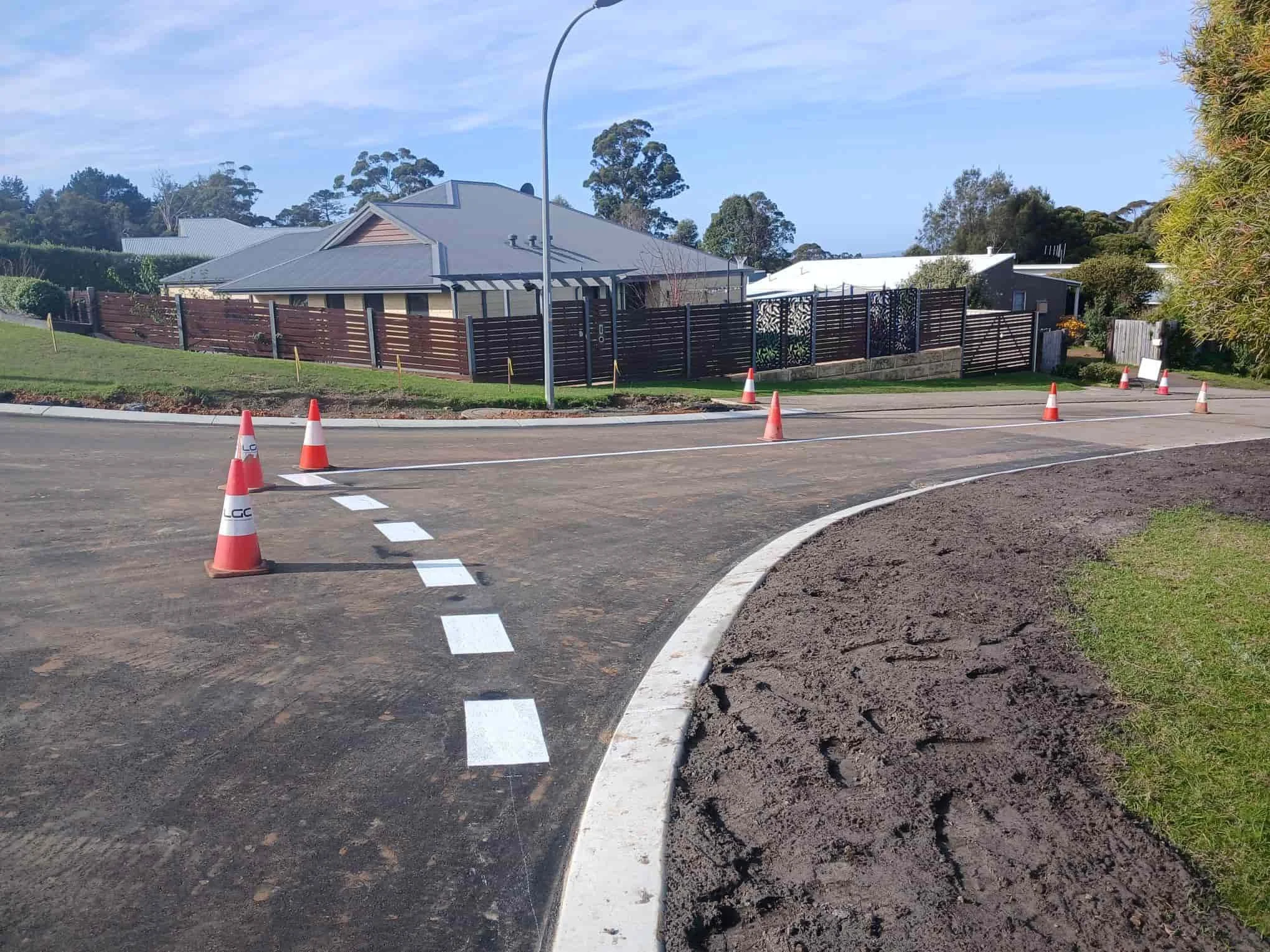 A residential street professional line marking, houses and trees in the background, and a curved curb in the foreground.