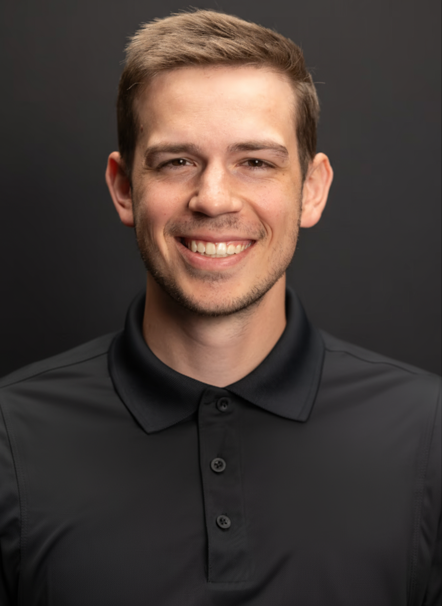 A smiling young man with light brown hair and a light complexion, wearing a black collared shirt, against a dark background.