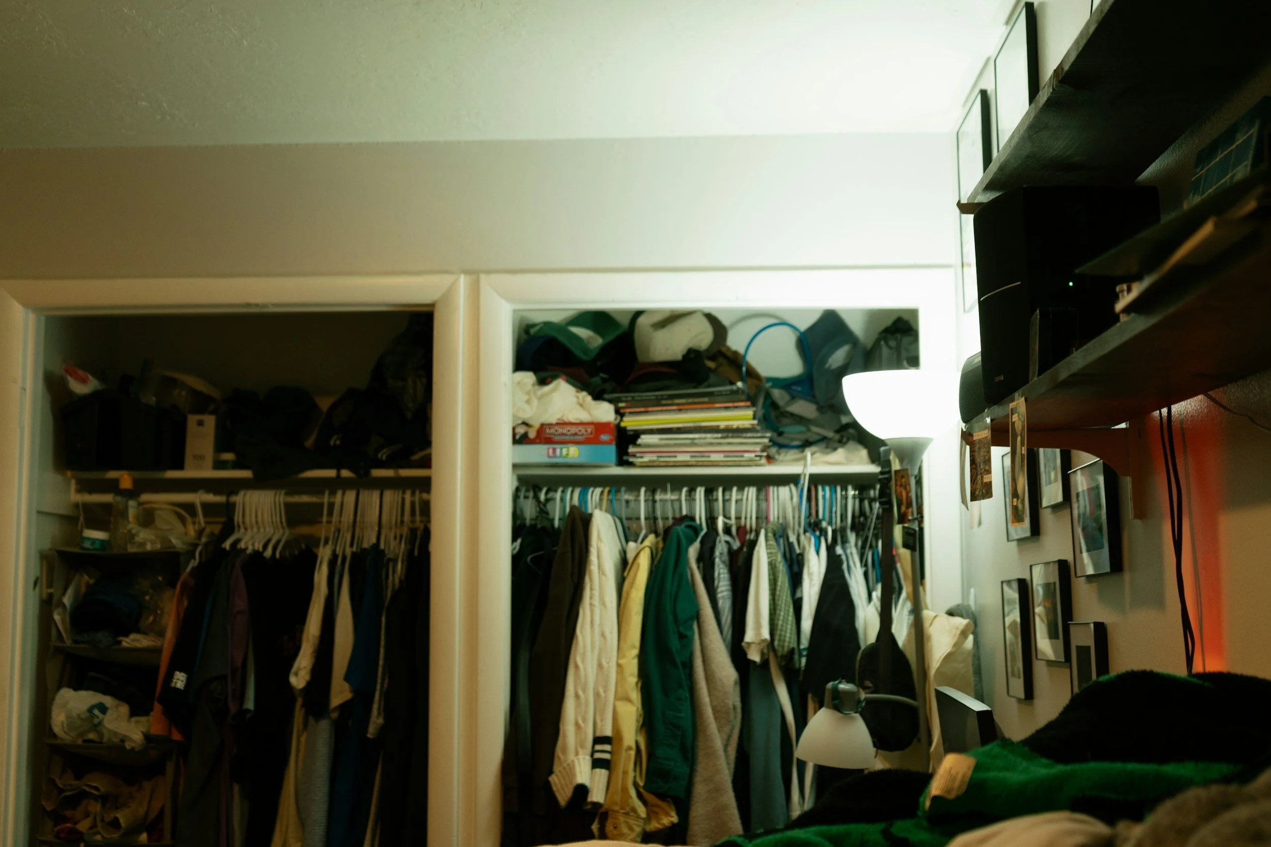 クローゼットに衣服やバッグが掛かっている部屋の写真。棚には本や小物、段ボール箱が置かれている。