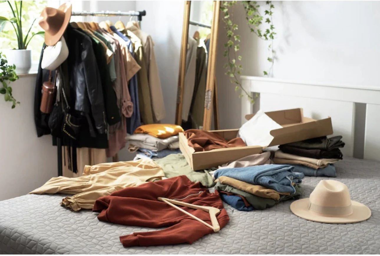 散らかった部屋で引き出しやクローゼットに衣服が散乱し、帽子やハンガーも置かれている