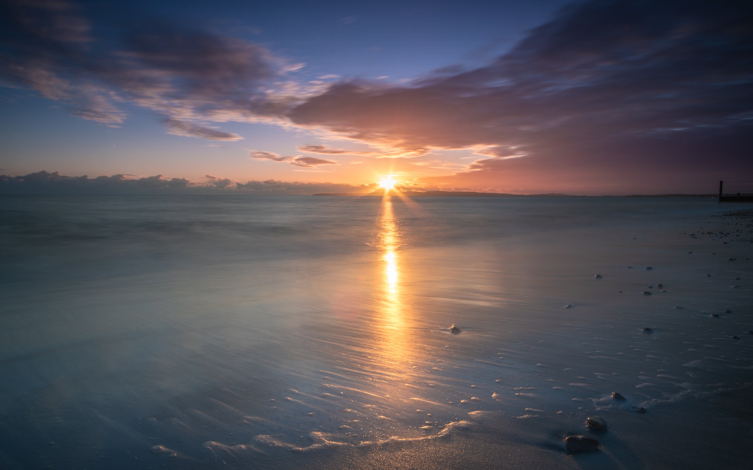The sun sets over a dreamy seascape as gentle waves lap against the shore.