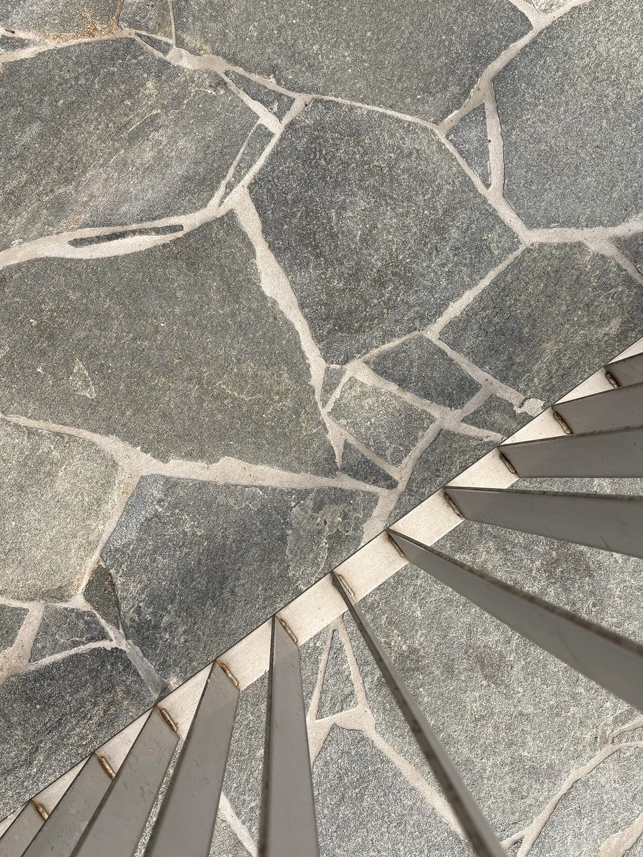Close-up of a gray stone tile floor with white grout lines and a part of a metal railing with vertical rods.