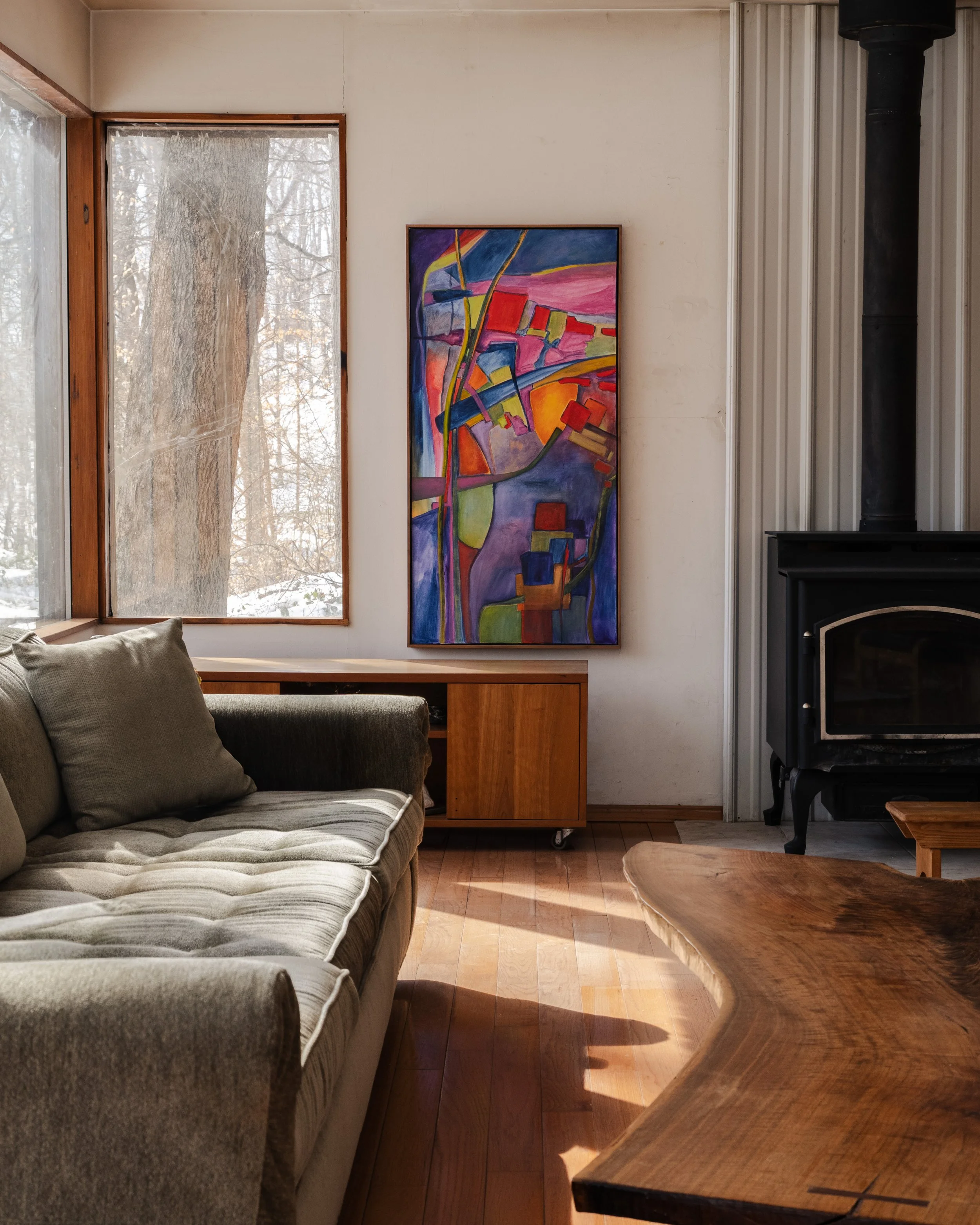 Interior editorial photography of McElroy House in Malvern PA, featuring modern living room vignette with wood stove, abstract artwork, and warm natural light.