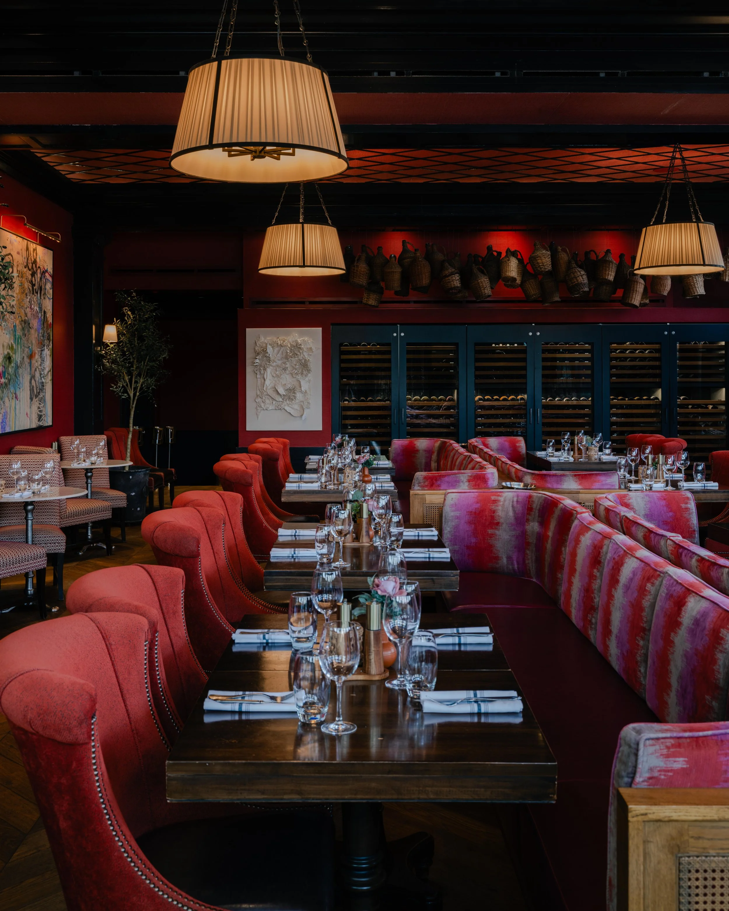 Modern restaurant interior with deep red walls, large abstract artwork, and warm pendant lighting above a marble table, styled dining setting with upholstered chairs and intimate ambiance, editorial interior design photography in the Philadelphia are