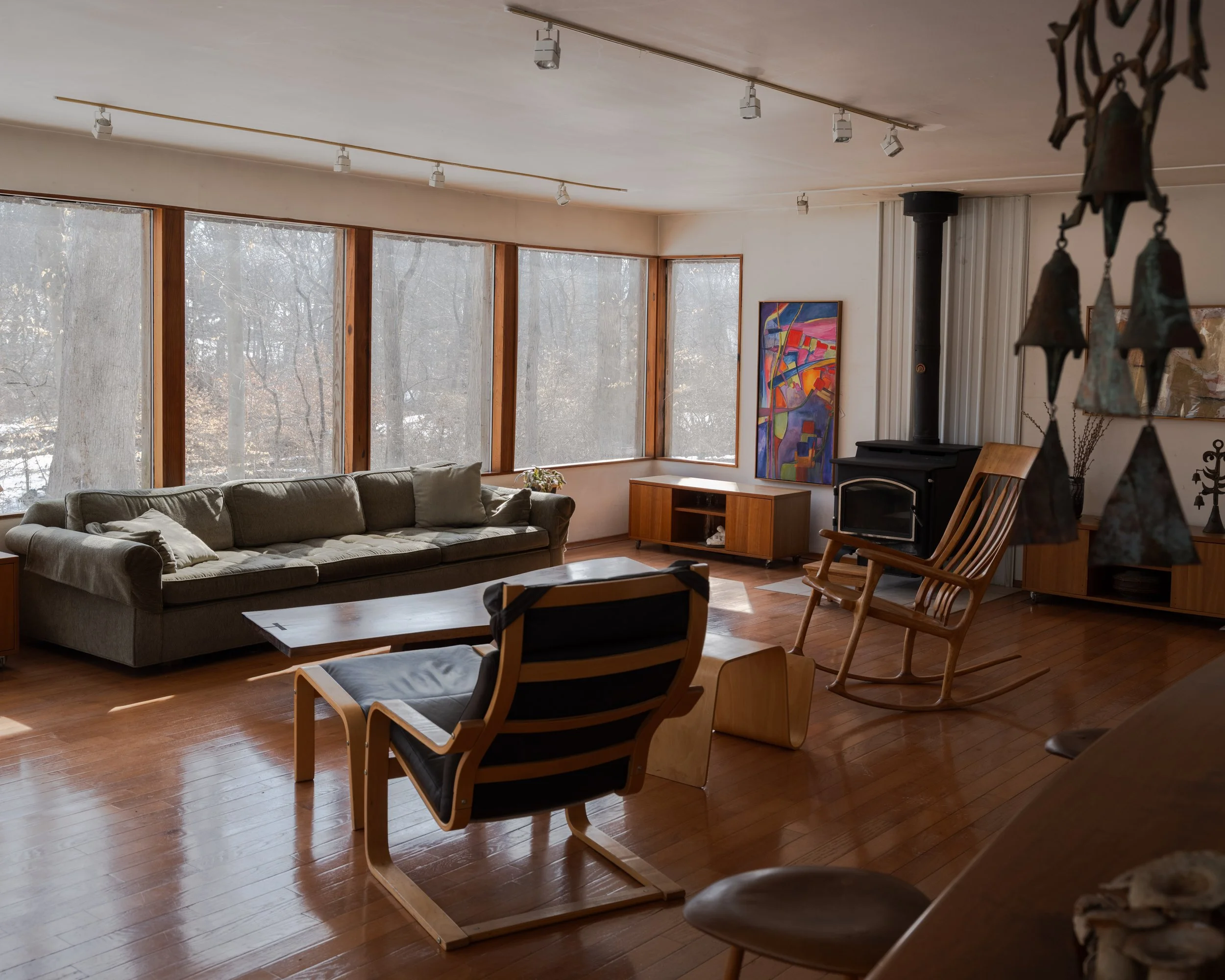 Interior editorial photography of McElroy House in Malvern PA, featuring modern living room with expansive windows, warm wood floors, and mid-century modern furniture.
