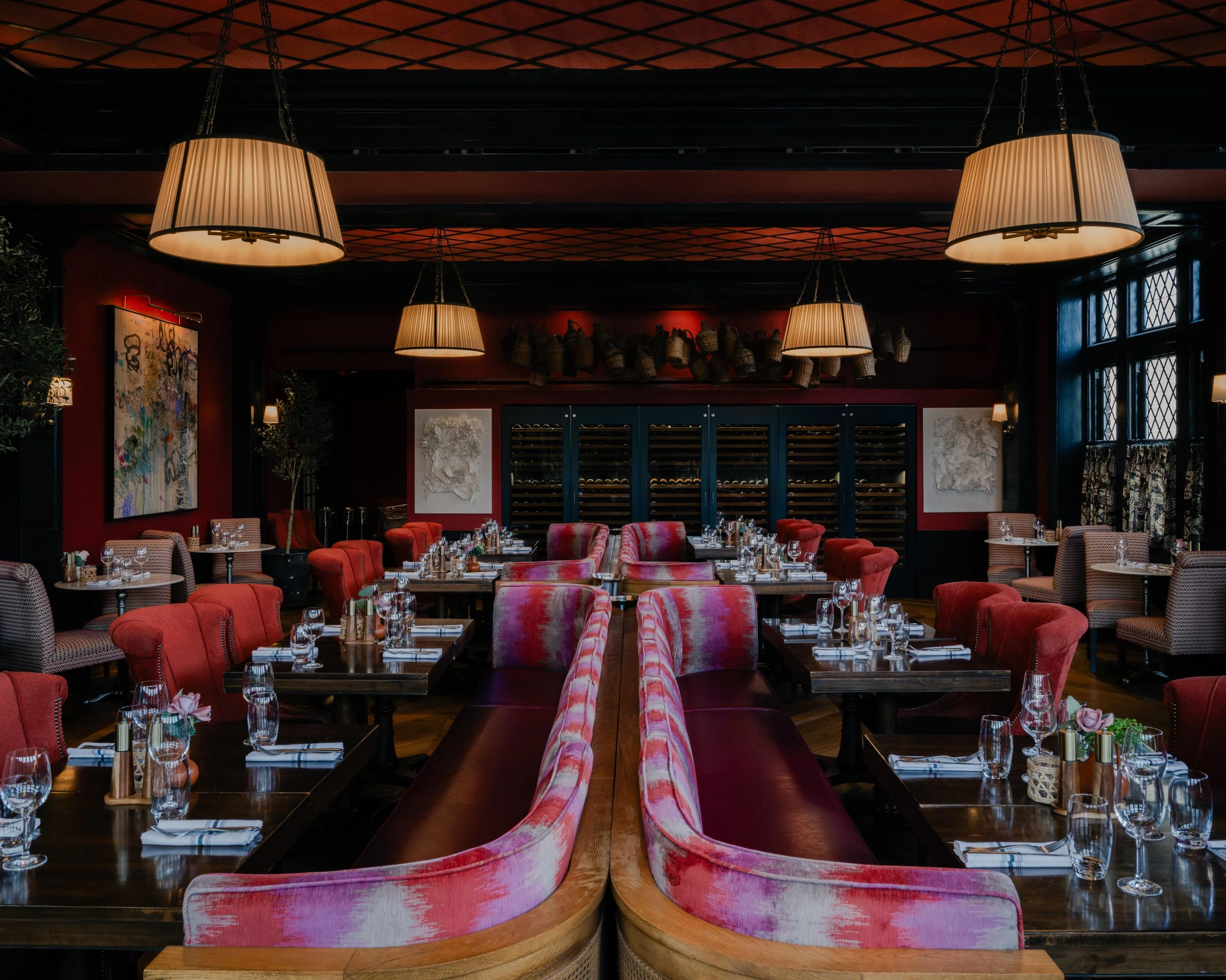 Modern restaurant interior with deep red walls, large abstract artwork, and warm pendant lighting above a marble table, styled dining setting with upholstered chairs and intimate ambiance, editorial interior design photography in the Philadelphia are