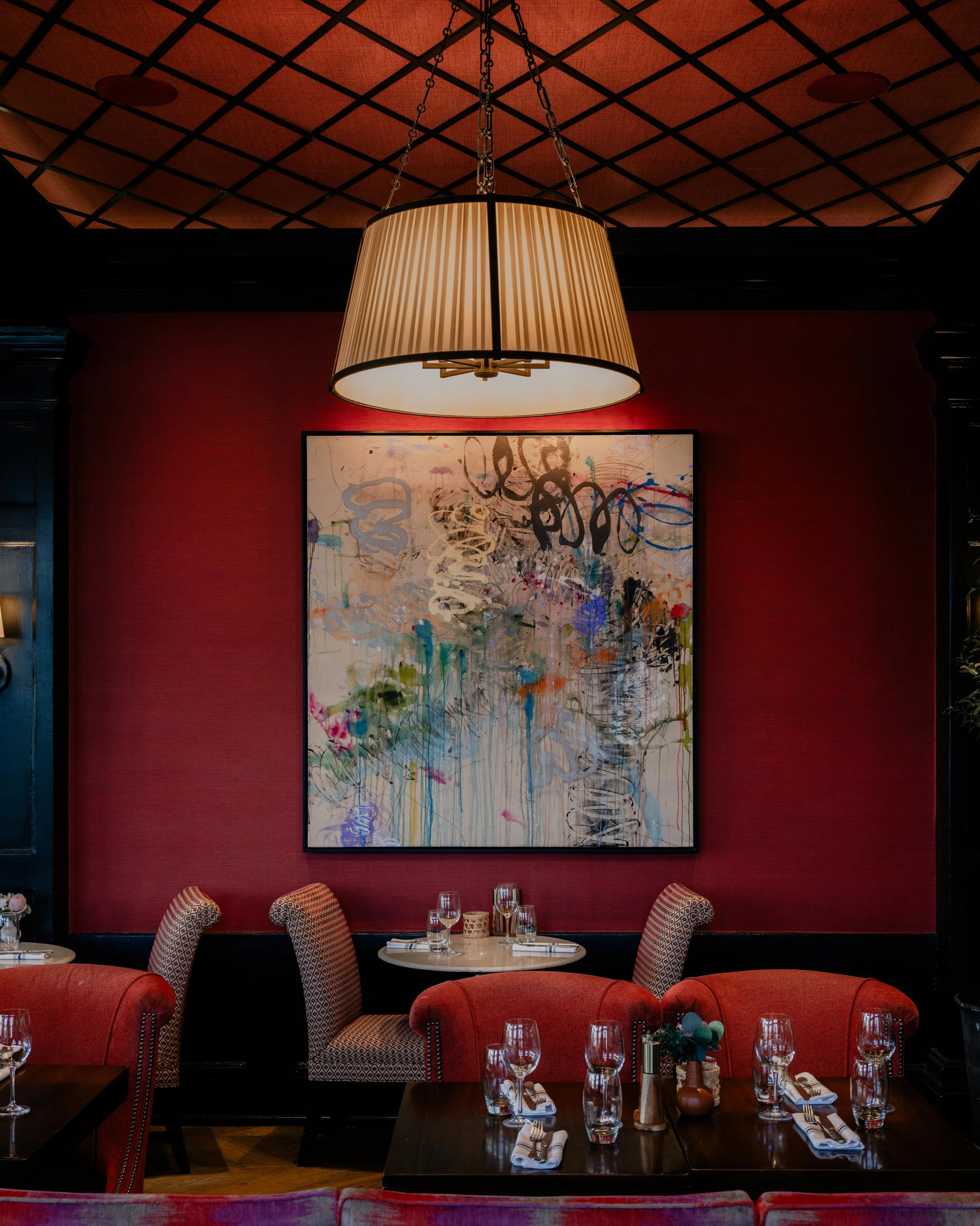 Modern restaurant interior with deep red walls, large abstract artwork, and warm pendant lighting above a marble table, styled dining setting with upholstered chairs and intimate ambiance, editorial interior design photography in the Philadelphia are