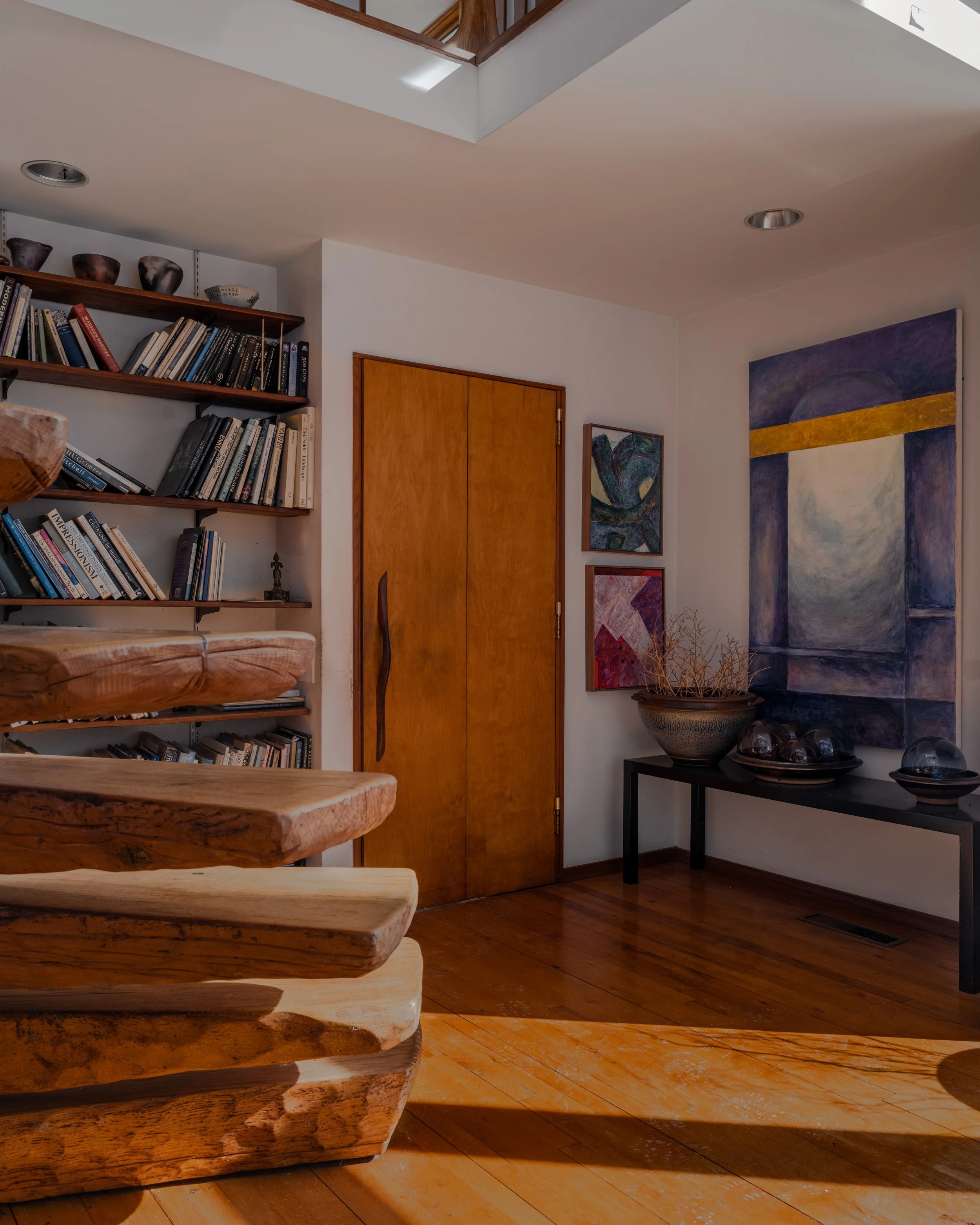 Interior editorial photography of McElroy House in Malvern PA, featuring sculptural wood staircase, built-in shelving, and curated artwork in warm natural light.