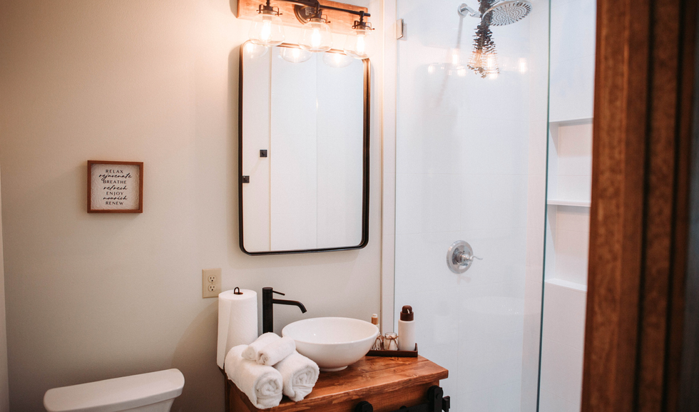 Bathroom with a wooden vanity, white vessel sink, black faucet, mirror, shower with glass door, and minimal decor.